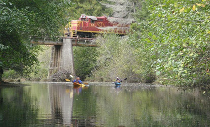 photo of skunk train going above the water with 2 kayakers paddling by.
