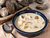 photo of clam chowder in a bowl with fresh clam shells sitting on the side.