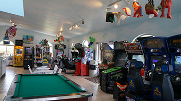 Fun at Emerald Dolphin photo showing a game room with pool table, video games, table and chairs. Pinatas for sale are hanging from the ceiling.