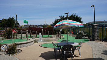 Photo showing golf course at the Emerald Dolphin Mini Golf. Table with umbrella and chairs.