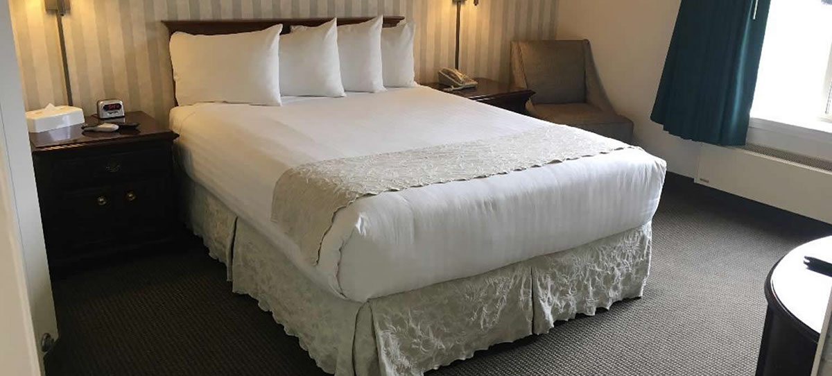 photo of our accessible room with queen size bed, night stands, lamps, sitting chair, alarm clock and direct dial phone. Large window for viewin