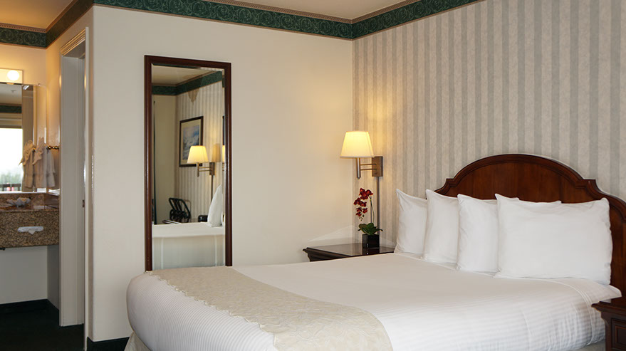 Photo showing queen bed, night stand with lamp, full length mirror and entrance to wash/ dressing area.