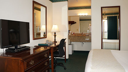 Photo showing queen bed, dresser, flat screen tv, writing desk with lamp and direct dial phone. Entrance to dressing/wash area.