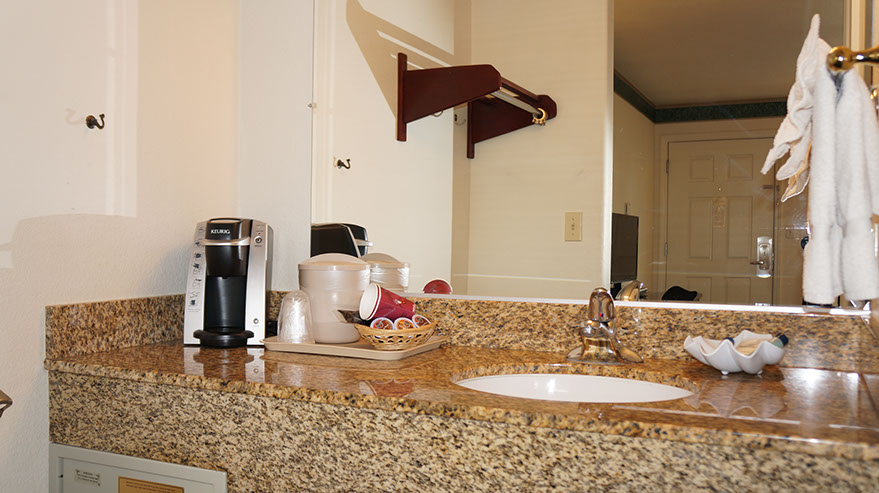 Photo showing large sink area with coffee maker and coffee, cups, bath essentials.