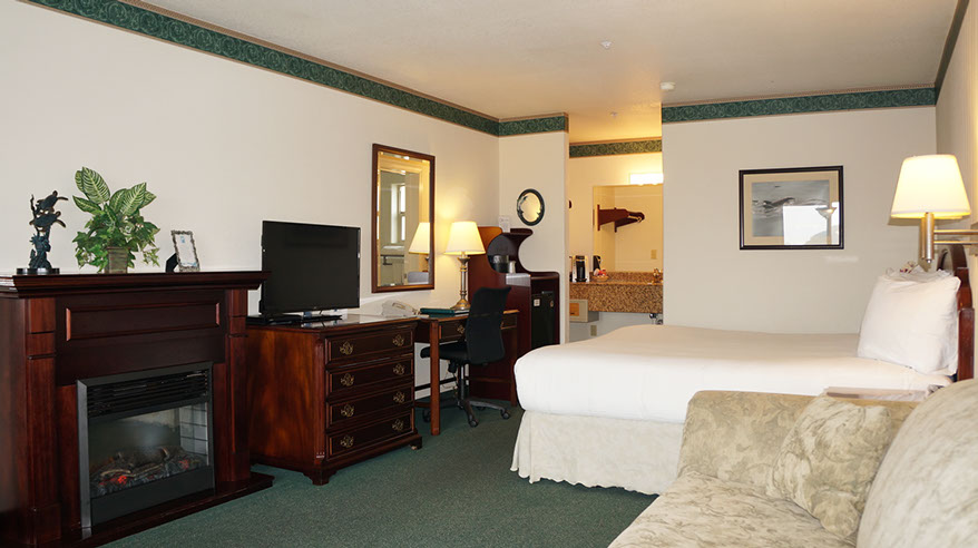 This spacious room is showing a European King Bed, Electric Fireplace, Chest of Drawers, Flat Screen TV, Writing Desk, Microwave and Mini Fridg.