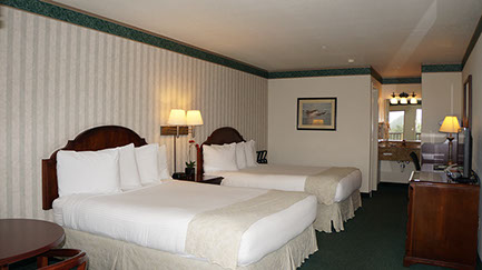 This family friendly 2 queen suite is showing 2 queen beds, dresser, writing desk, night stand with lamps and separate dressing area.