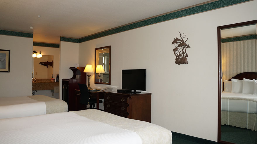 photo showing 2 queen beds, dresser, flatscreen tv, writing desk, microwave, mini fridg and separate lighted dressing/wash area.