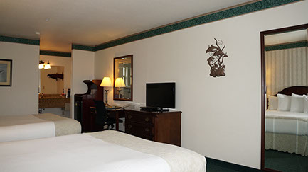 photo showing 2 queen beds, dresser, flatscreen tv, writing desk, microwave, mini fridg and separate lighted dressing/wash area.