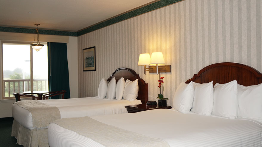 Photo showing 2 queen beds, night stand with double lamps, table with 2 chairs next to a large viewing window.