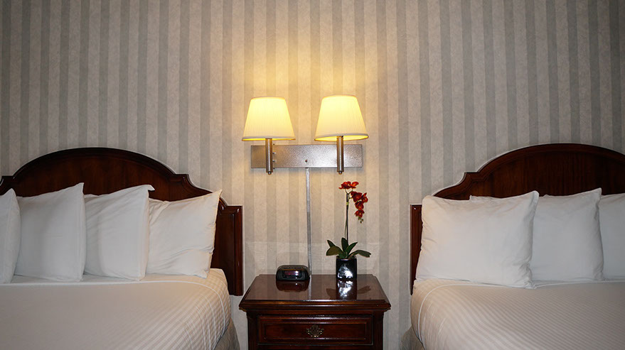 Photo showing 2 queen beds with night stand, double lamps and an alarm clock.