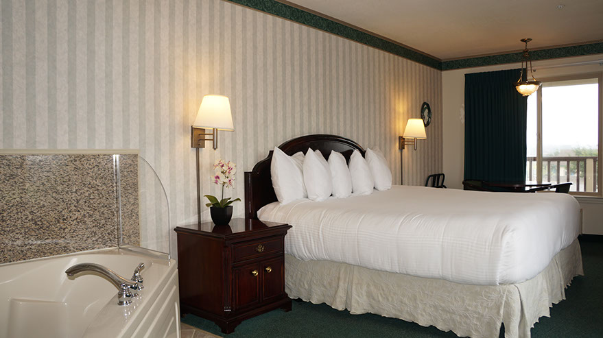 European King Size Bed guest room photo showing King bed, jacuzzi tub, night stand, lamps and large window.