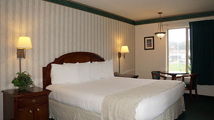 Photo showing alternate angle of European King bed, night stands with lamps, table with 2 chairs with large window.