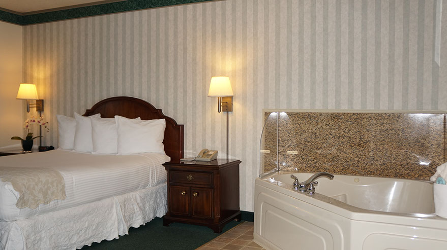 Photo shows a different angle with jacuzzi tub that seats 2, quen bed, night stands with lamps, direct dial phone. 