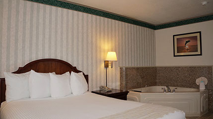 Photo shows queen bed, night stand with lamp, direct dial phone, and jacuzzi tub that seats 2.
