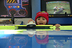Child playing air hockey at Ed's Mini Golf and Arcade, located next to Emerald Dolphin in Fort Bragg CA