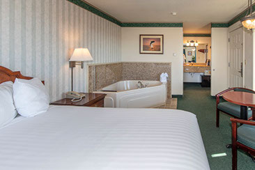 Photo shows a different angle with jacuzzi tub that seats 2, quen bed, night stands with lamps, direct dial phone. 