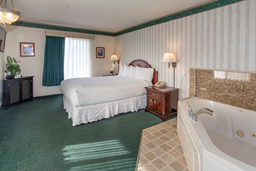 Photo shows a different angle with jacuzzi tub that seats 2, quen bed, night stands with lamps, direct dial phone. 