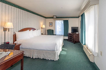 Our King Suite showing a European King bed, table with 2 chairs, dresser, night stands and large window.
