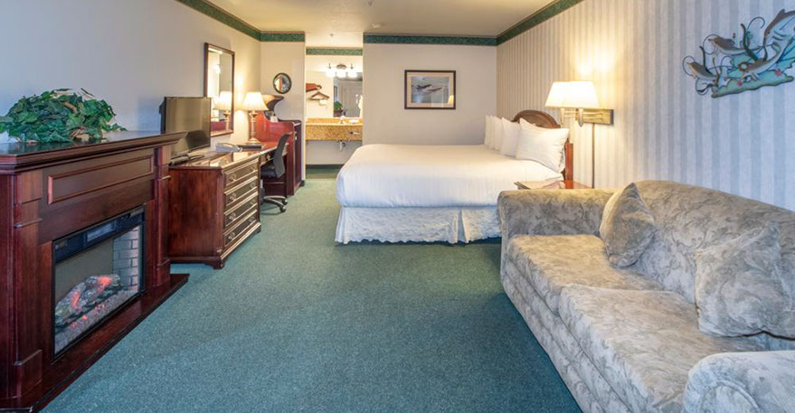 This spacious room is showing a European King Bed, Electric Fireplace, Chest of Drawers, Flat Screen TV, Writing Desk, Microwave and Mini Fridg.