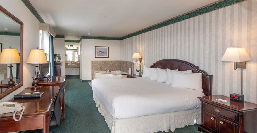 European King Size Bed guest room. Photo showing King Bed, Jacuzzi Tub, Writing Desk with lamp and phone.